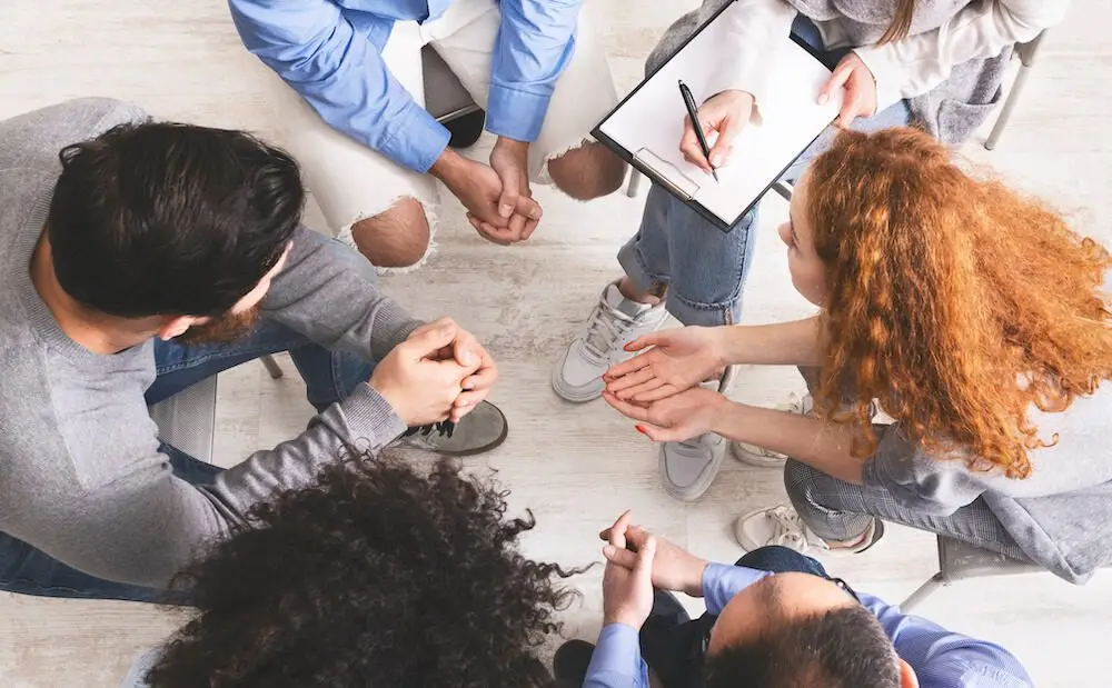 People gathered in a group during therapy while the therapist takes notes