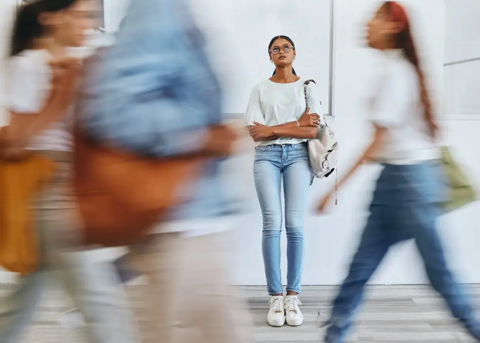 A young woman standing alone at school feeling overwhelmed and worried.