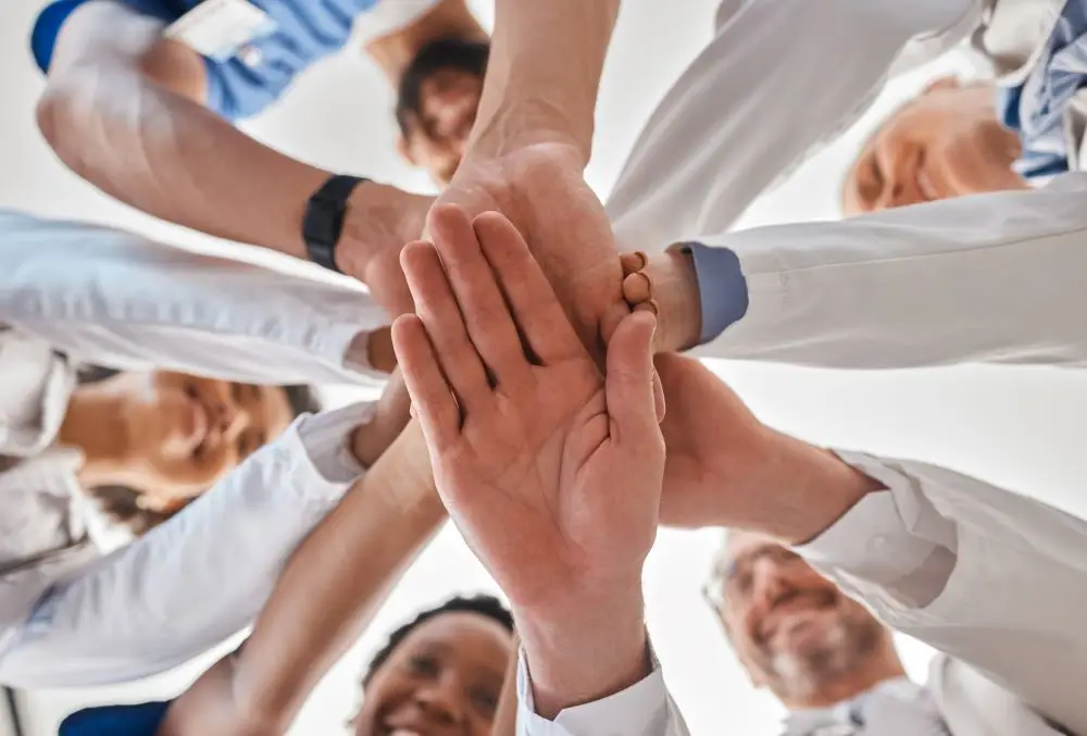 A group of medical professionals showing their support for their team and their patients by putting their hands together in cooperation.