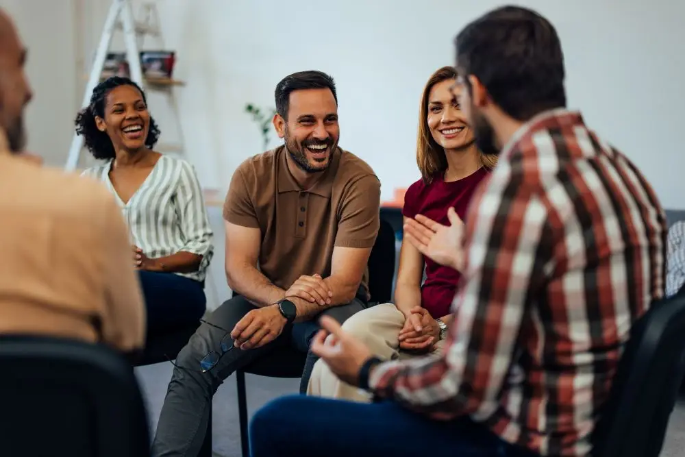 A group of people in therapy discussing their experiences and helping one another with building social skills.