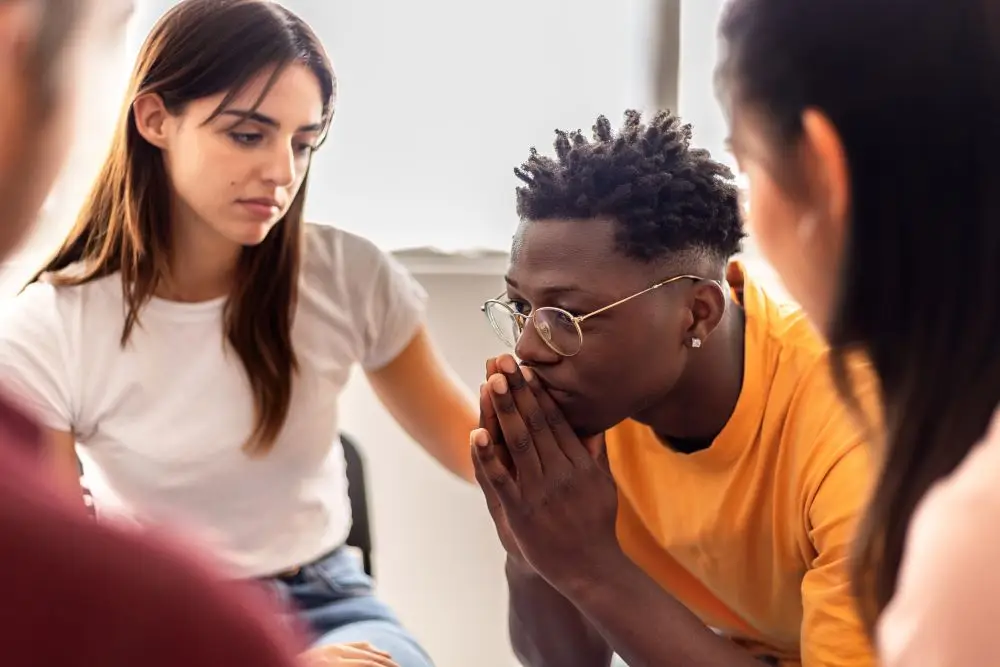 A young man showing signs of stress and anxiousness when being surrounded by a group of peers.