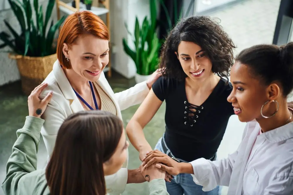 Psychologist and diverse group of multiethnic women joining hands during motivation coaching, moral support and mental wellness.