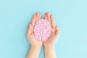 Two hands holding a drawing of a brain in the center.
